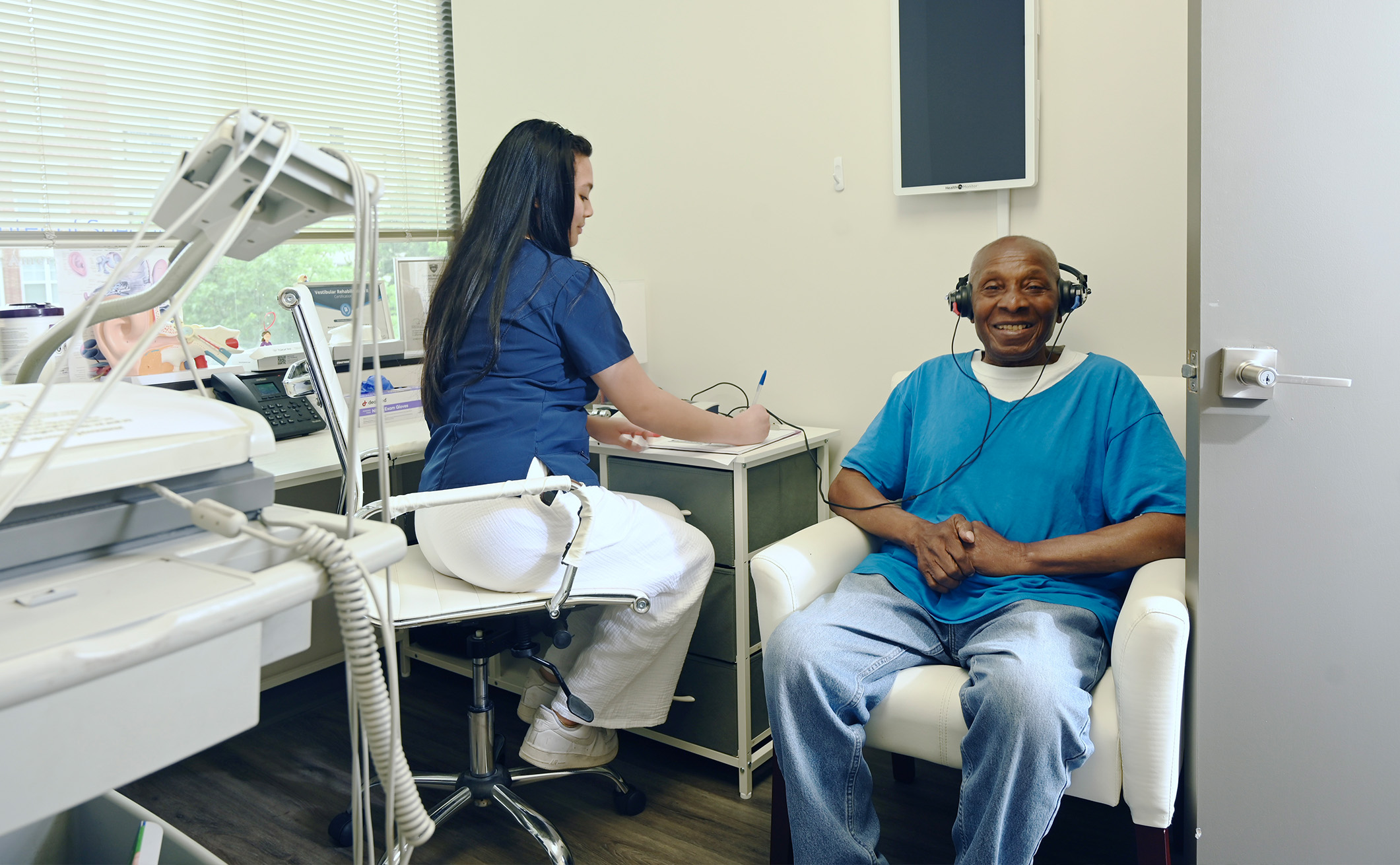 A dentist's office with a man sitting in a chair receiving dental care from a woman standing at a counter with a dental device.